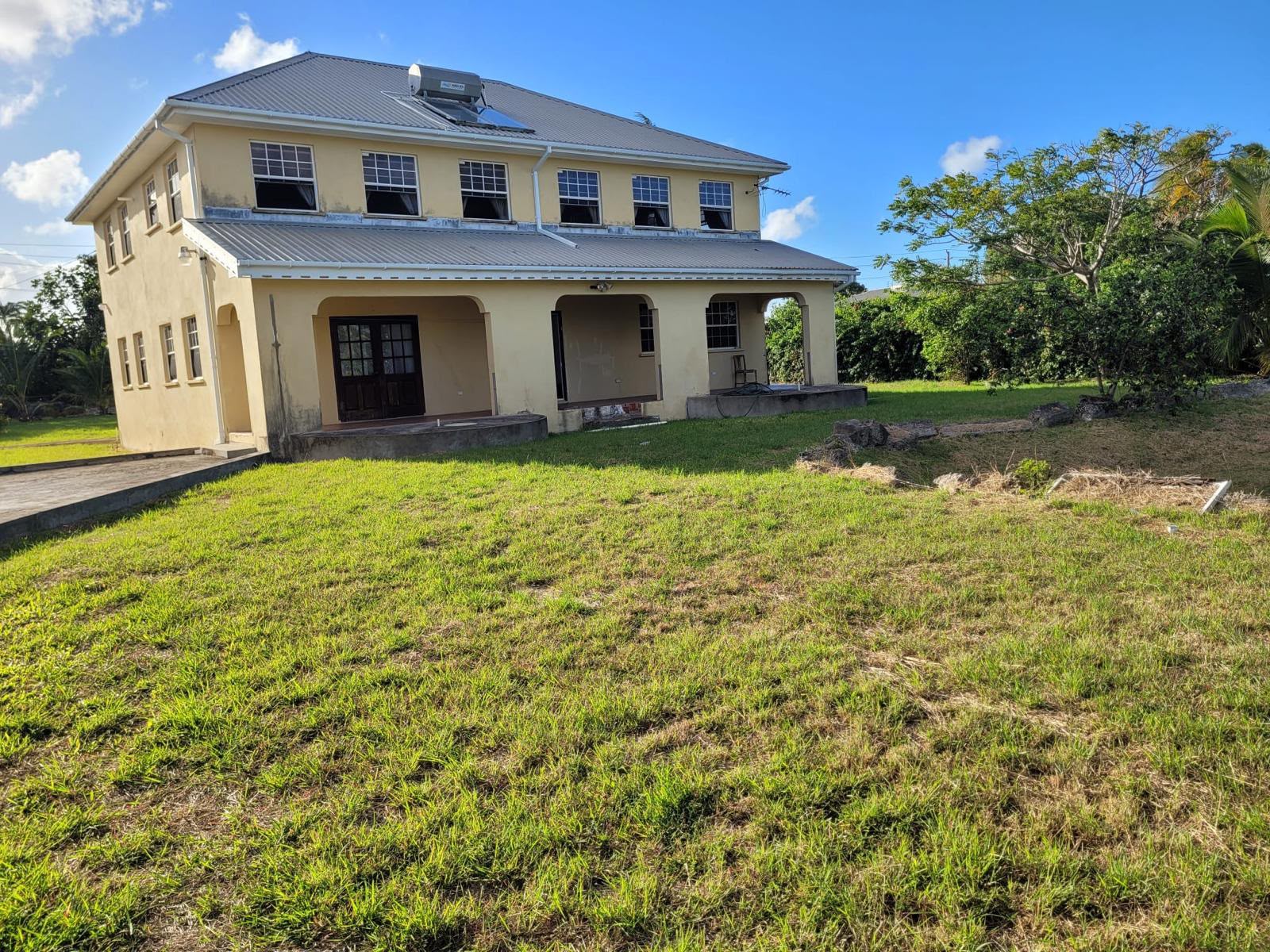 The back of Lyngros: a two-storey yellow house with an arched veranda, set on a wide lawn